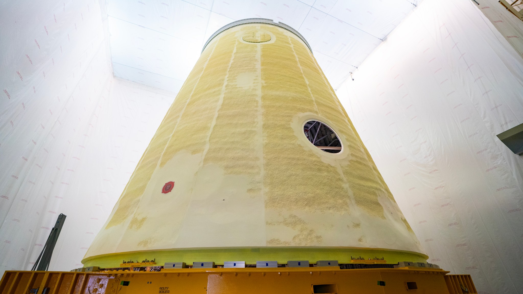 The cone-shaped launch vehicle stage adapter, seen in yellow, is in a production area.