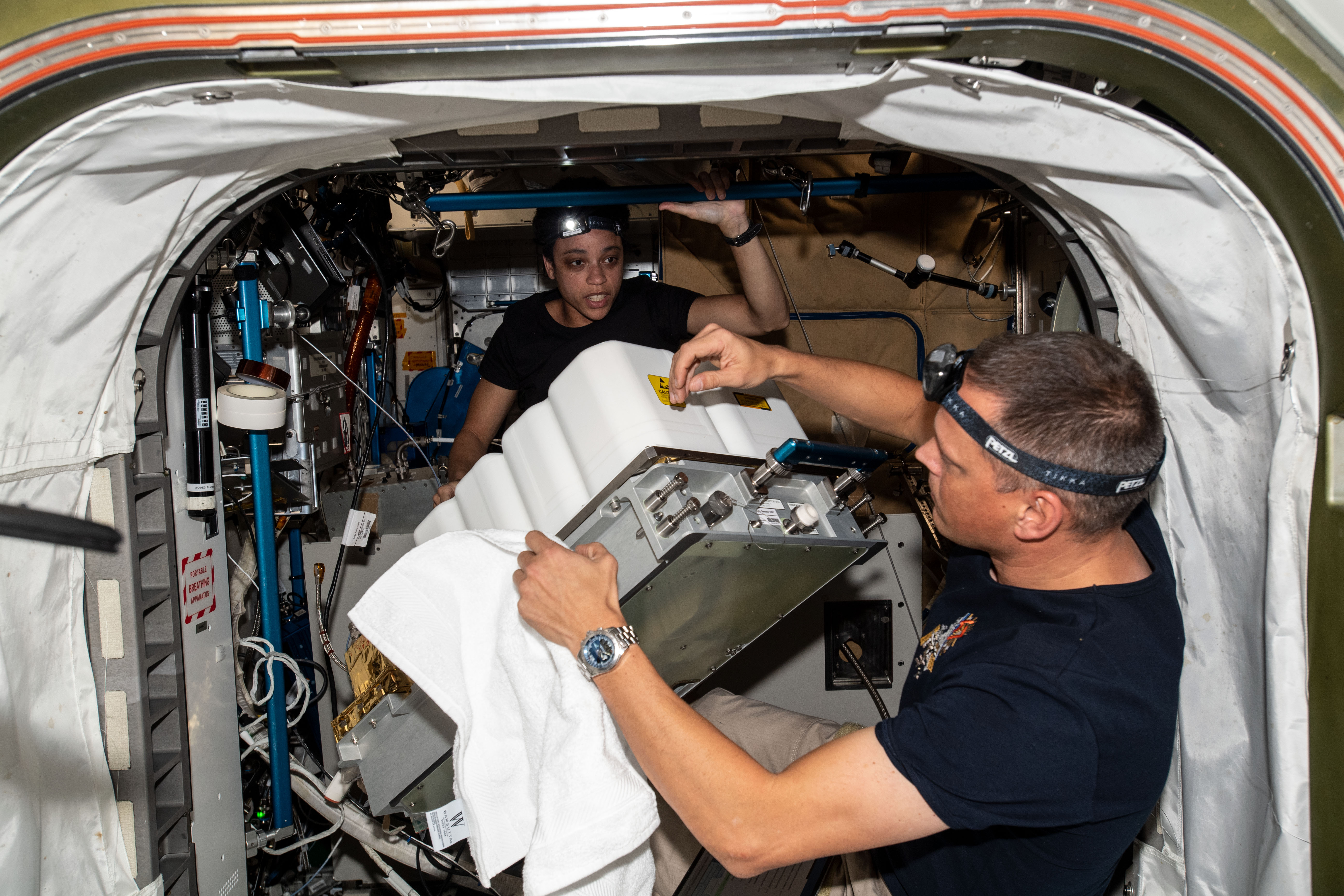 NASA astronauts and Expedition 67 Flight Engineers Bob Hines and Jessica Watkins perform maintenance inside the Tranquility module's Waste and Recycling System abaord the International Space Station.