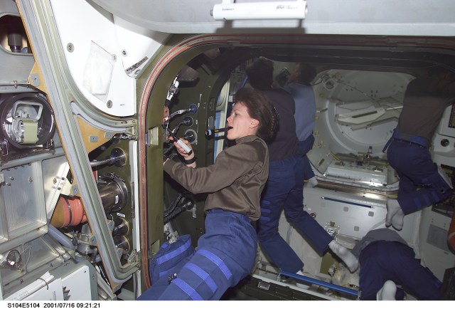 Janet L. Kavandi, STS-104 mission specialist, connects cables and hoses from the newly installed Quest Airlock to Unity Node 1. Other STS-104 and Expedition Two crewmembers are visible in the background working in the Airlock.