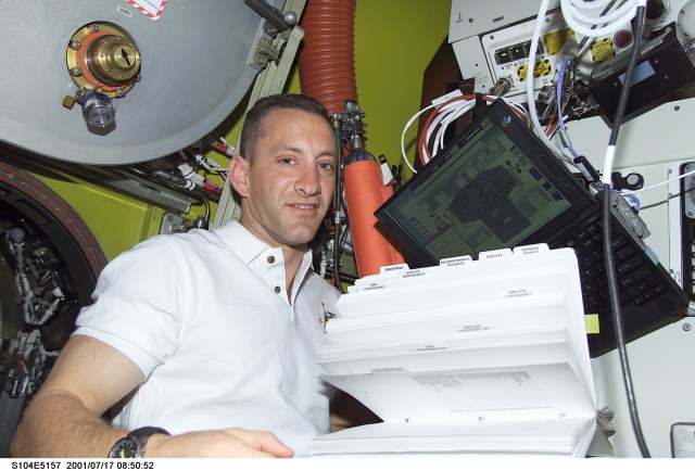 Astronaut Charles O. Hobaugh, STS-104 pilot, looks over a reference manual in the Quest Airlock aboard the International Space Station (ISS). The image was recorded with a digital still camera.