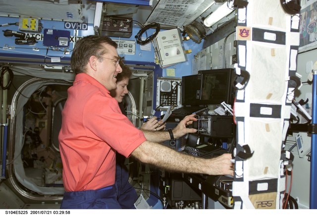 A crew member used a digital still camera to take a picture of members of the Expedition Two crew at work in the Destiny laboratory. Within the final three weeks of their habitation aboard the International Space Station (ISS), astronauts James S. Voss and Susan J. Helms, flight engineers, both performed important maneuvers with the Canadarm2, Space Station Remote Manipulator System (SSRMS), during the STS-104 mission. Cosmonaut Yury V. Usachev, Expedition Two commander, is out of frame.