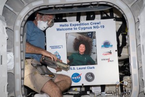 NASA astronaut and Expedition 69 Flight Engineer Stephen Bowen wears personal protective equipment (PPE) shortly after entering the Northrop Grumman Cygnus space freighter. The PPE protects an astronaut from eye contact with and breathing in any dust or debris that may have dislodged during the spacecraft's ascent to orbit. Bowen poses with a portrait of NASA astronaut Laurel Clark, whom the Cygnus cargo craft is named after, who perished aboard space shuttle Columbia during its return to Earth on Feb. 1, 2003.