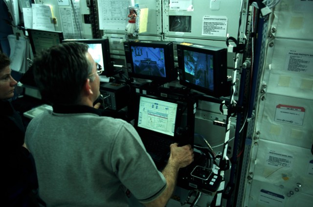 Astronauts James S. Voss and Susan J. Helms work at the controls of the new Canadian-built space station robotic arm as a historic "first" takes place in Earth orbit. The robotics "handshake in space" occurred as the Canadarm2 transferred its launch cradle over to Endeavour's Canadian-built remote manipulator system (RMS) robotic arm, with astronaut Chris A. Hadfield, mission specialist representing the Canadian Space Agency (CSA), at the controls on the flight deck of the shuttle.