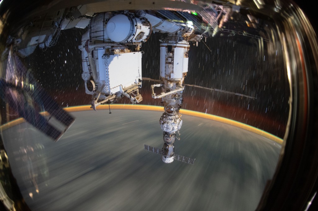 This long-duration photograph shows the Earth 259 miles below a soaring International Space Station. In the foreground, is the Soyuz MS-21 crew ship docked to the Prichal docking module which is itself attached to the Nauka multipurpose laboratory module.