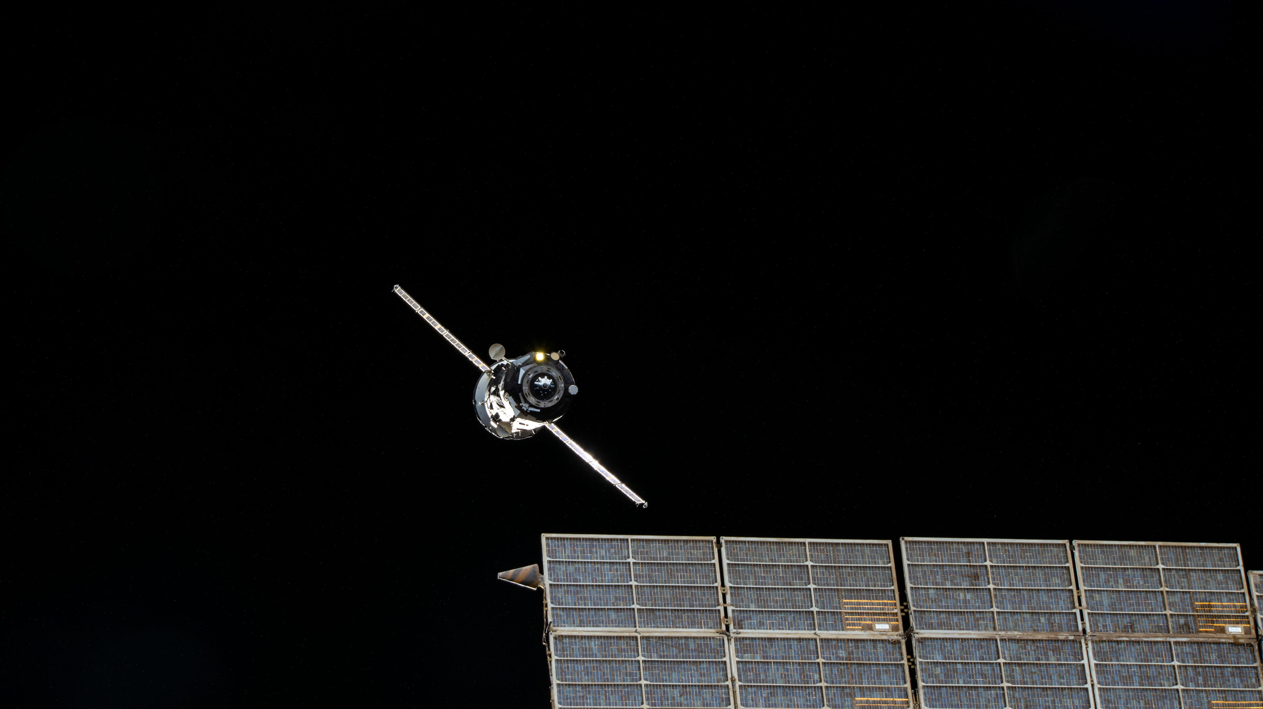 The ISS Progress 79 resupply ship from Roscosmos is pictured departing the vicinity of the International Space Station after undocking from the Zvezda service module's rear port. In the foreground, one of two solar arrays attached to Zvezda is pictured.