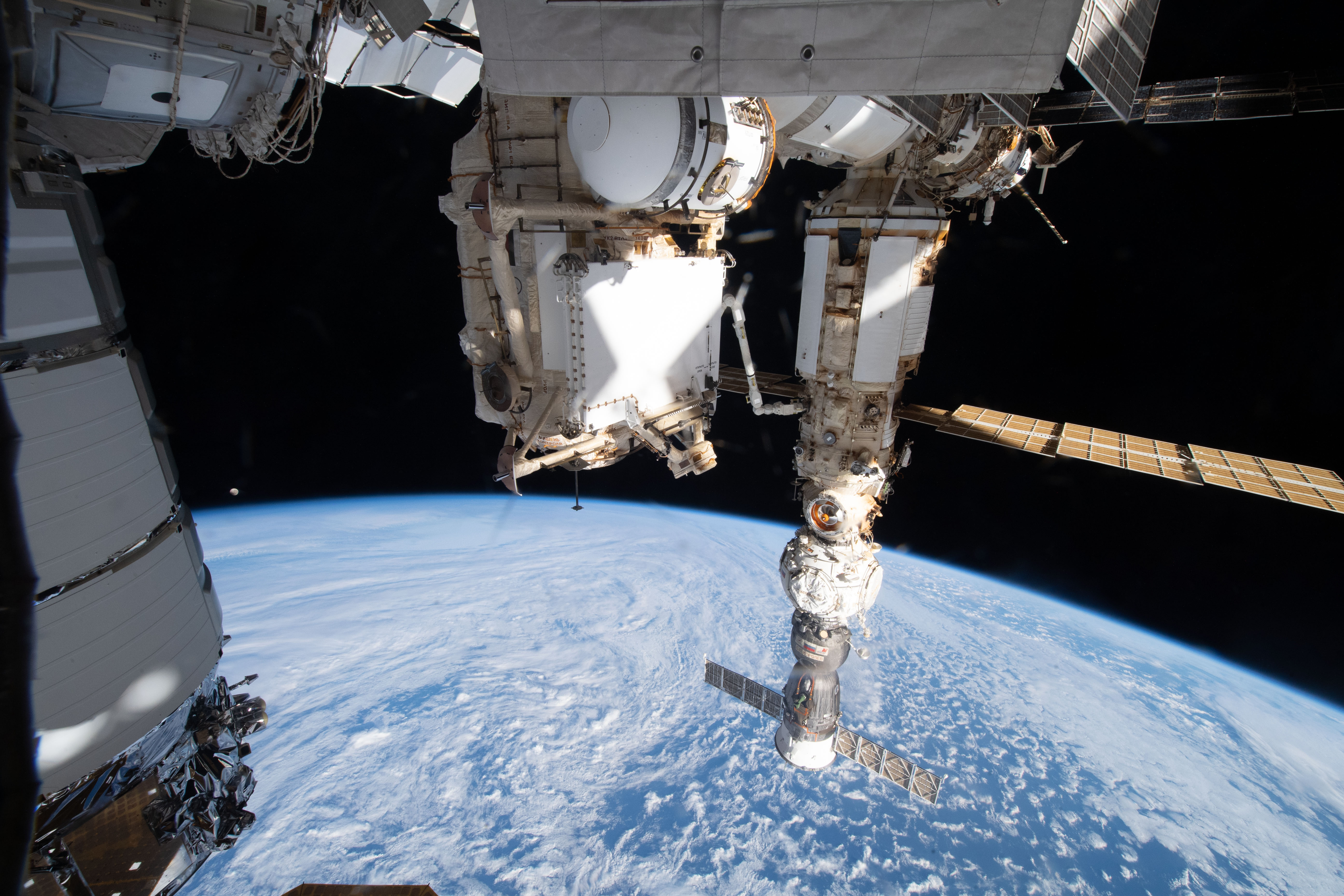 The Moon, with Earth's shadow draping across it during a lunar eclipse and pictured just above the horizon, is dwarfed in between U.S. and Russian International Space Station components. At left, is the U.S. Northrop Grumman Cygnus space freighter, with Russia's Rassvet module at center, and a trio of Russian station elements attached to each other, including (from bottom to top) the Soyuz MS-21 crew ship, the Prichal docking module, and the Nauka multipurpose laboratory module. The station was orbitng 273 miles above the southern Indian Ocean off the coast of the French Southern and Antarctic Lands.
