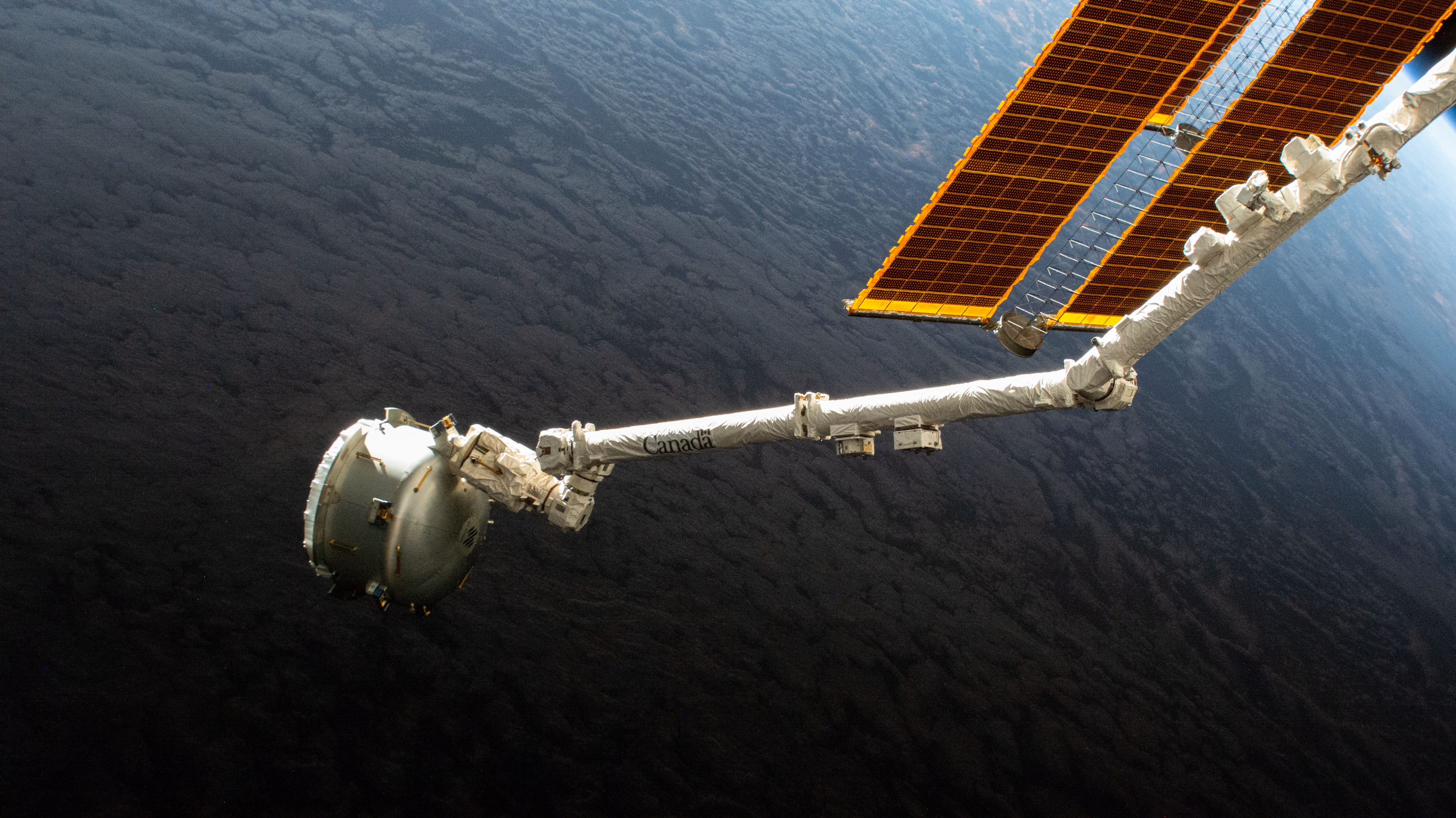 The Nanoracks Bishop Airlock is pictured in the grips of the Canadarm2 robotic arm as it is positioned away from the International Space Station. The commercial platform was being maneuvered prior to jettisoning a trash container for a fiery, but safe disposal above Earth's atmopshere. Bishop is a multi-faceted airlock attached to the Tranquility module used not only to discard trash, but also to host research payloads, deploy satellites, and serve as a testbed for a variety of space technologies.