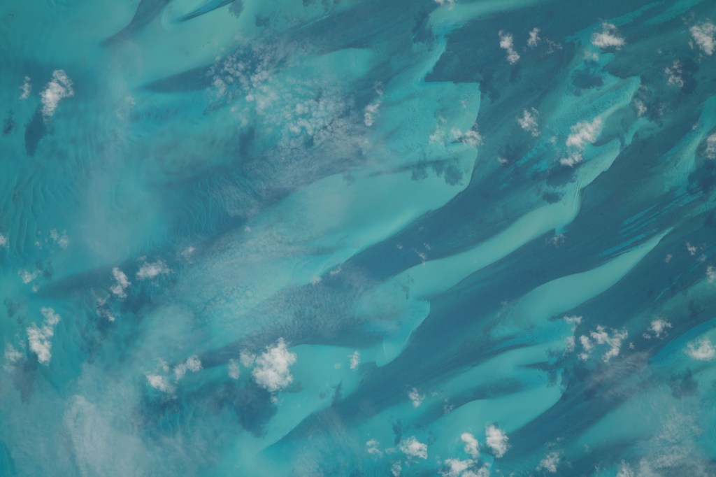 Small scatters of clouds lightly hang over the dark blue and turquoise waters of the Bahamas as the International Space Station soared 262 miles above.