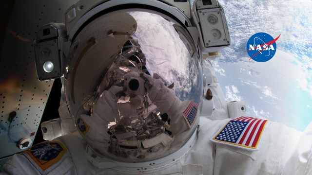 Up close image of astronaut's helmet and arm while floating in space.