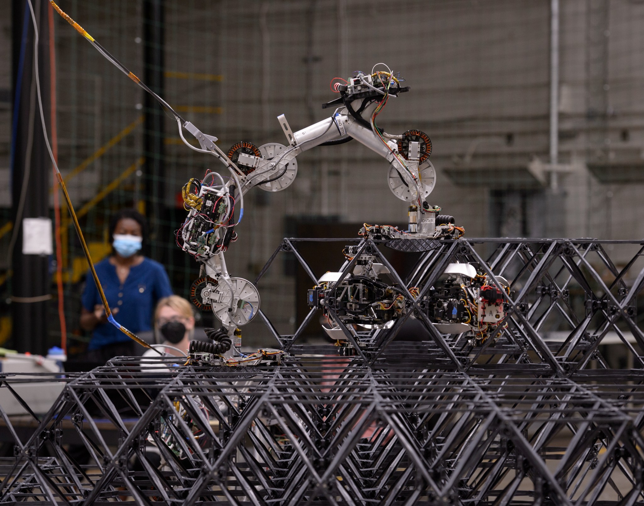 Two NASA researchers watch small robots assembling building blocks into a structure in a laboratory.