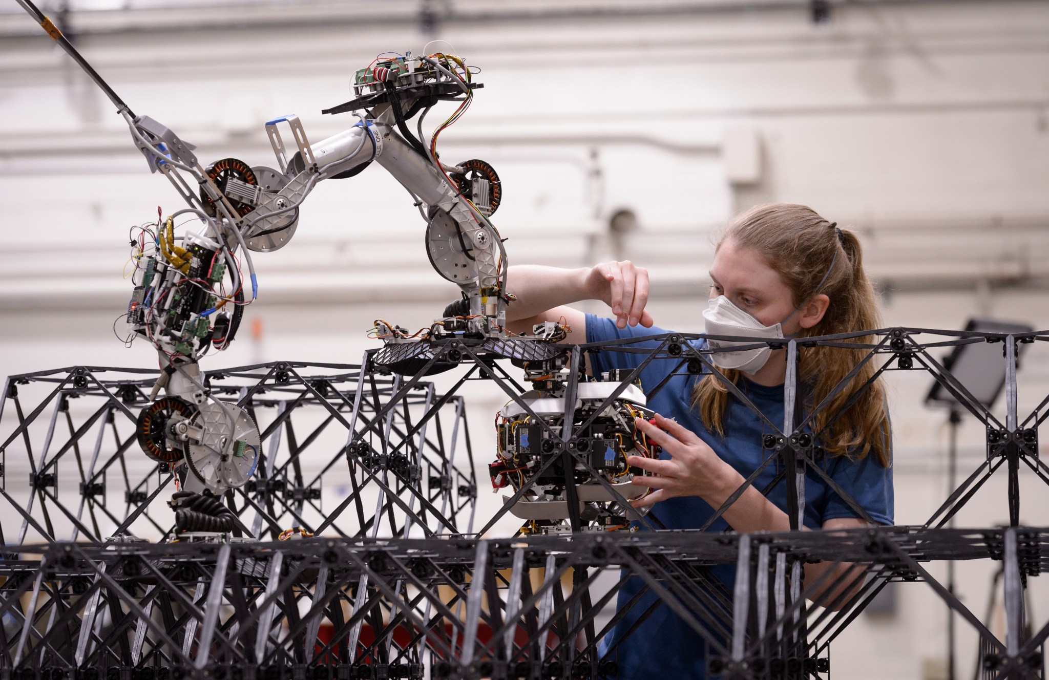 A NASA researcher closely examines a small robot that bolts building blocks to a structure.