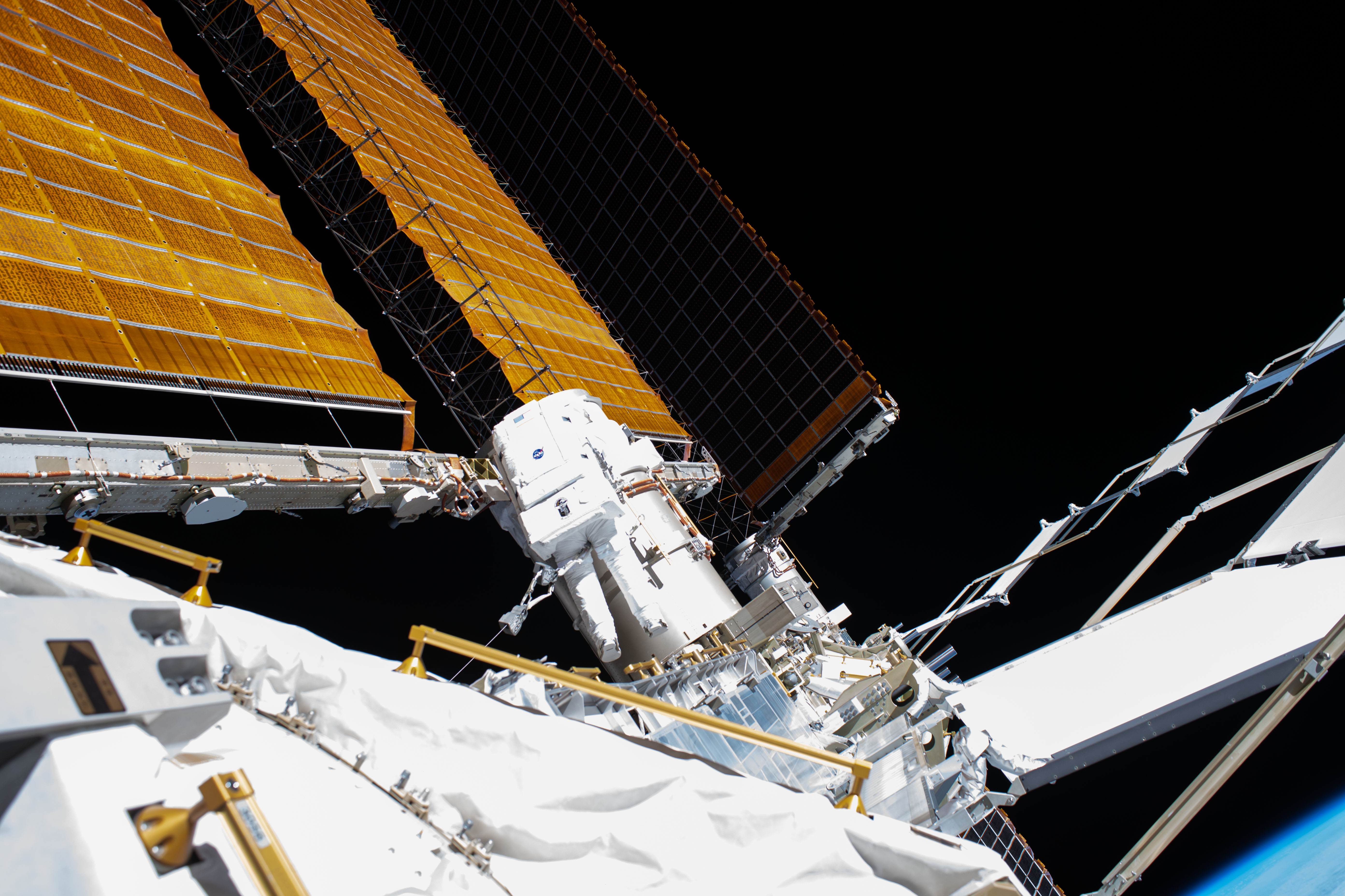NASA astronaut and Expedition 63 Flight Engineer Bob Behnken (center) works during a six-hour and one-minute spacewalk to swap an aging nickel-hydrogen battery for a new lithium-ion battery on the International Space Station's Starboard-6 truss structure. Protruding diagonally towards the upper left are the station's main solar arrays which are the length of basketball court.