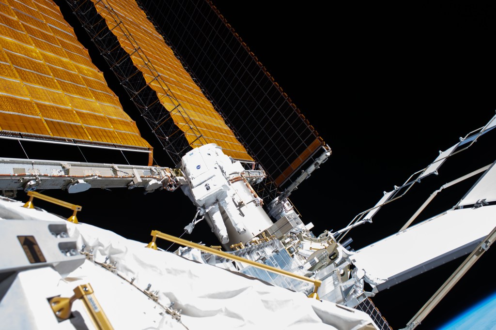 NASA astronaut and Expedition 63 Flight Engineer Bob Behnken (center) works during a six-hour and one-minute spacewalk to swap an aging nickel-hydrogen battery for a new lithium-ion battery on the International Space Station's Starboard-6 truss structure. Protruding diagonally towards the upper left are the station's main solar arrays which are the length of basketball court.