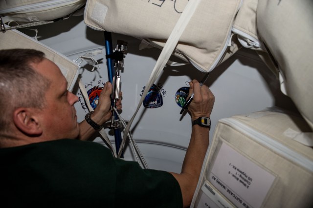 iss068e012476 (Oct. 5, 2022) --- NASA astronaut and Expedition 68 Flight Engineer Bob Hines signs his name around the OFT-2 (Orbital Flight Test-2) mission insignia sticker affixed to the Harmony module's vestibule. Hines was aboard the International Space Station when Boeing's CST-100 Starliner spacecraft docked to Harmony's forward port on May 19, 2022, for a six-day uncrewed test mission.