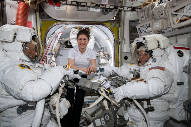 NASA astronaut Christina Koch (center) assists spacewalkers Nick Hague (left) and Anne McClain in their U.S. spacesuits shortly before they begin the first spacewalk of their careers. Hague and McClain would work outside in the vacuum of space for six hours and 39 minutes to upgrade the International Space Station's power storage capacity.