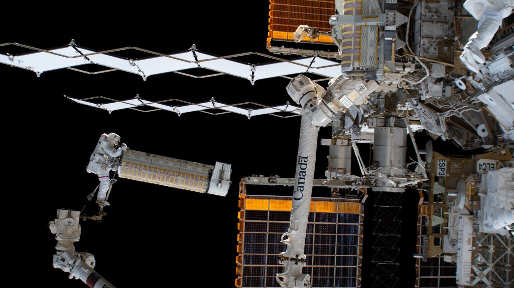 iss068e026403 (Dec. 3, 2022) --- NASA astronaut and Expedition 68 Flight Engineer Josh Cassada holds a roll-out solar array as he rides the Canadarm2 robotic arm toward the Starboard-4 truss segment installation site.