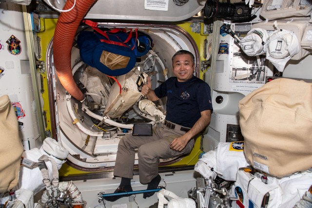 iss068e044024 (Jan. 31, 2023) --- Expedition 68 Flight Engineer Koichi Wakata of the Japan Aerospace Exploration Agency (JAXA) is pictured inside the International Space Station's Quest airlock while organizing spacewalk tools and hardware. In the foreground, are two Extravehicular Mobility Units (EMUs), or spacesuits, with their helmets covered and the lower arms and gloves detached.