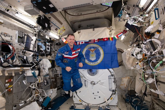 NASA astronaut Nick Hague poses for a portrait with the insignia of the United States Air Force behind him aboard the International Space Station.