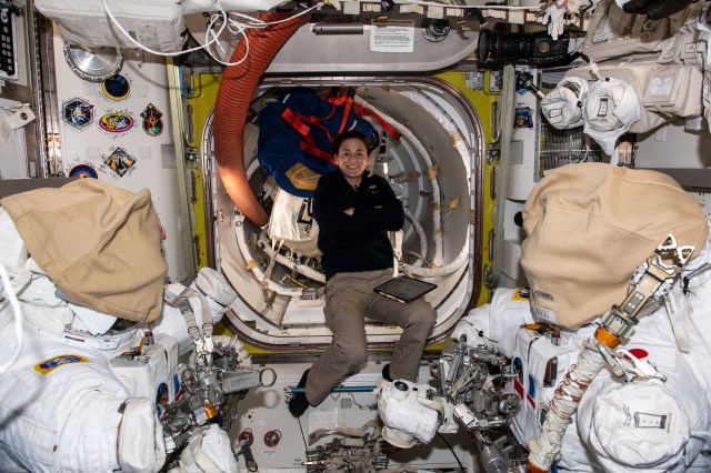 iss068e044025 (Jan. 31, 2023) --- NASA astronaut and Expedition 68 Flight Engineer Nicole Mann is pictured inside the International Space Station's Quest airlock while organizing spacewalk tools and hardware. In the foreground, are two Extravehicular Mobility Units (EMUs), or spacesuits, with their helmets covered and the lower arms and gloves detached.