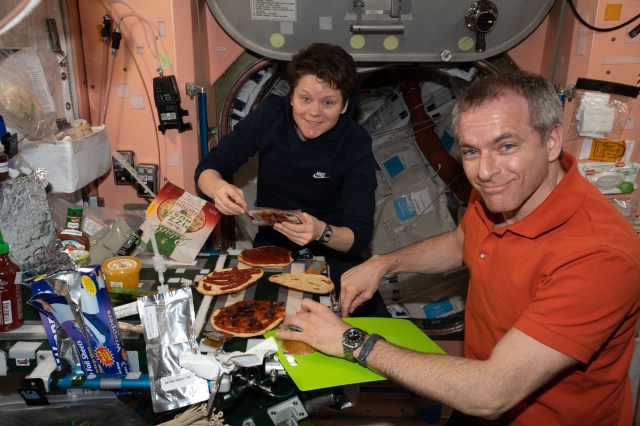 NASA astronaut Anne McClain and David Saint-Jacques of the Canadian Space Agency prepare to enjoy personal-size pizzas with all the toppings and fixings you would find in an ordinary kitchen on Earth.