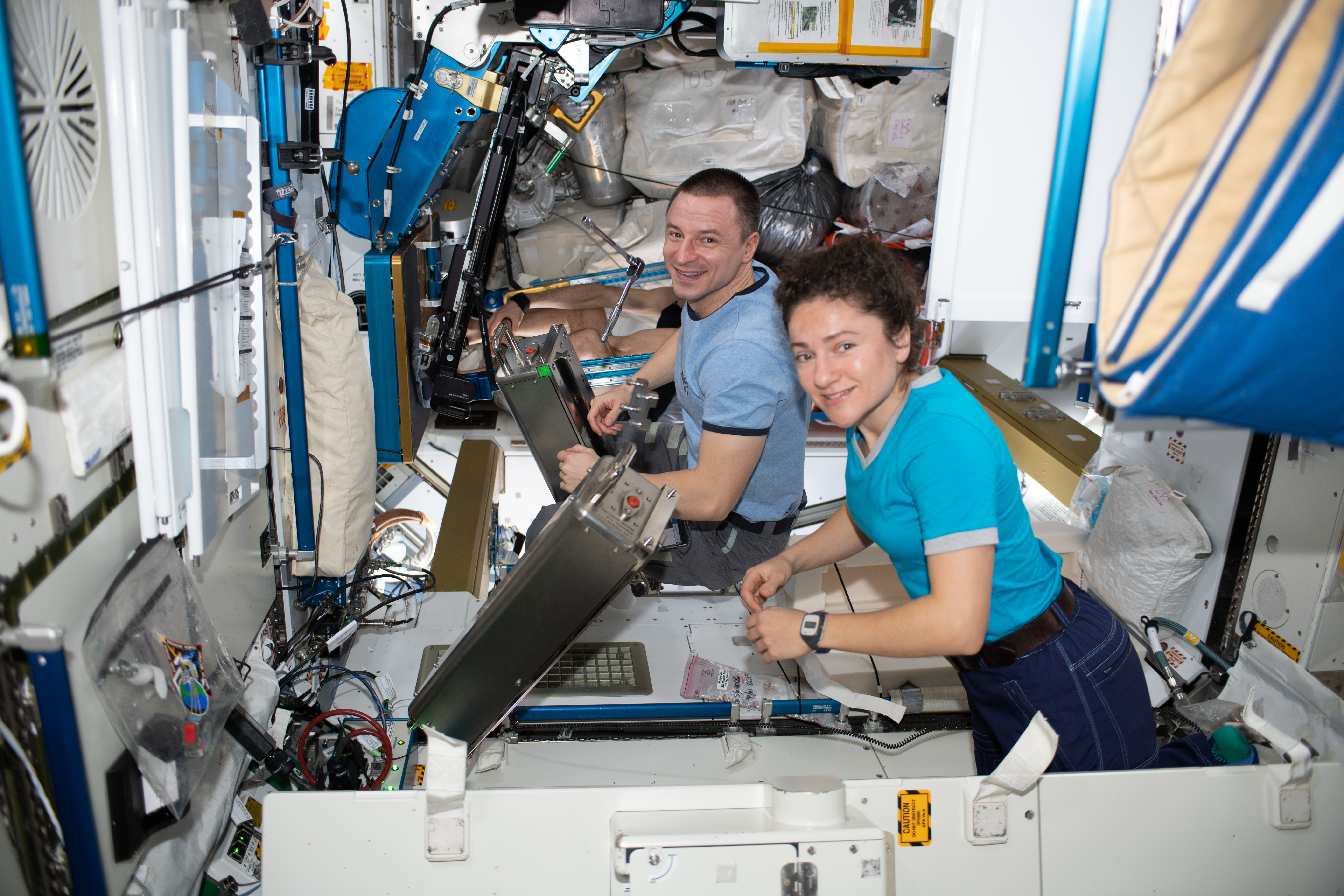 NASA astronauts Jessica Meir and Andrew Morgan, both Expedition 61 Flight Engineers, work on orbital plumbing tasks inside the Waste and Hygiene Compartment aboard the International Space Station's Tranquility module.