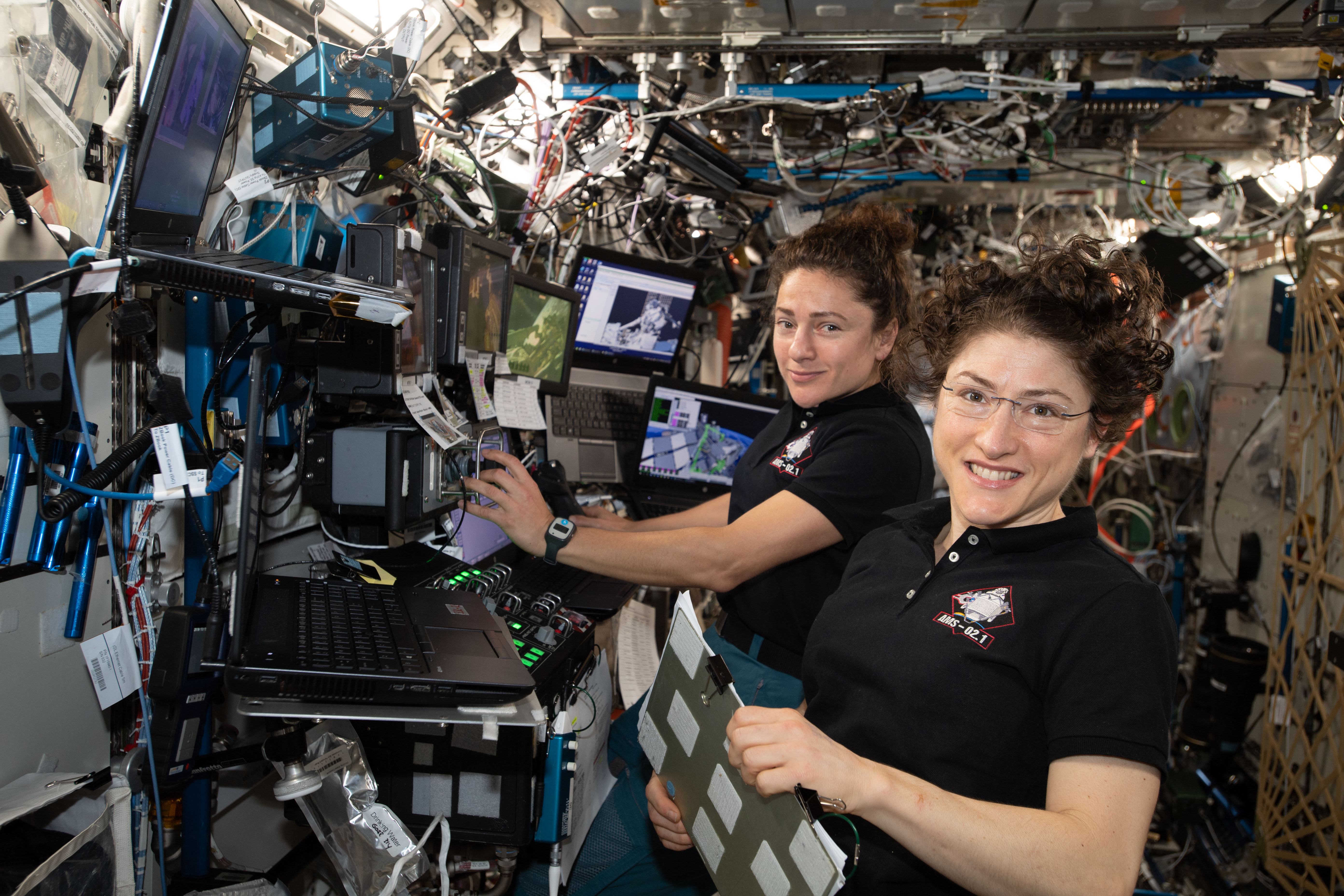 NASA astronauts (from left ) Jessica Meir and Christina Koch are at the robotics workstation controlling the Canadarm2 robotic arm to support the first spacewalk to repair the Alpha Magnetic Spectrometer (AMS), the International Space Station's cosmic particle detector. Astronauts Luca Parmitano of ESA (European Space Agency) and Andrew Morgan of NASA worked six hours and 39 minutes in the vacuum of space during the first of at least four planned AMS repair spacewalks.
