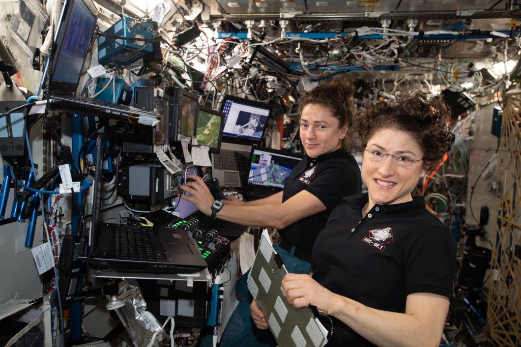 NASA astronauts (from left ) Jessica Meir and Christina Koch are at the robotics workstation controlling the Canadarm2 robotic arm to support the first spacewalk to repair the Alpha Magnetic Spectrometer (AMS), the International Space Station's cosmic particle detector. Astronauts Luca Parmitano of ESA (European Space Agency) and Andrew Morgan of NASA worked six hours and 39 minutes in the vacuum of space during the first of at least four planned AMS repair spacewalks.