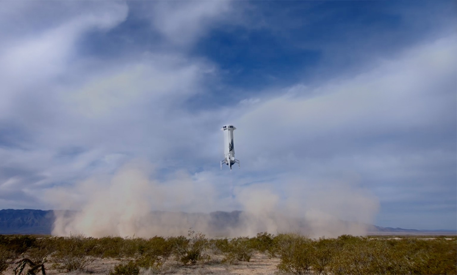 Reusable rocket coming in for a vertical landing, kicking up a plume of dust from the arid ground. The blue sky is full of wispy clouds.