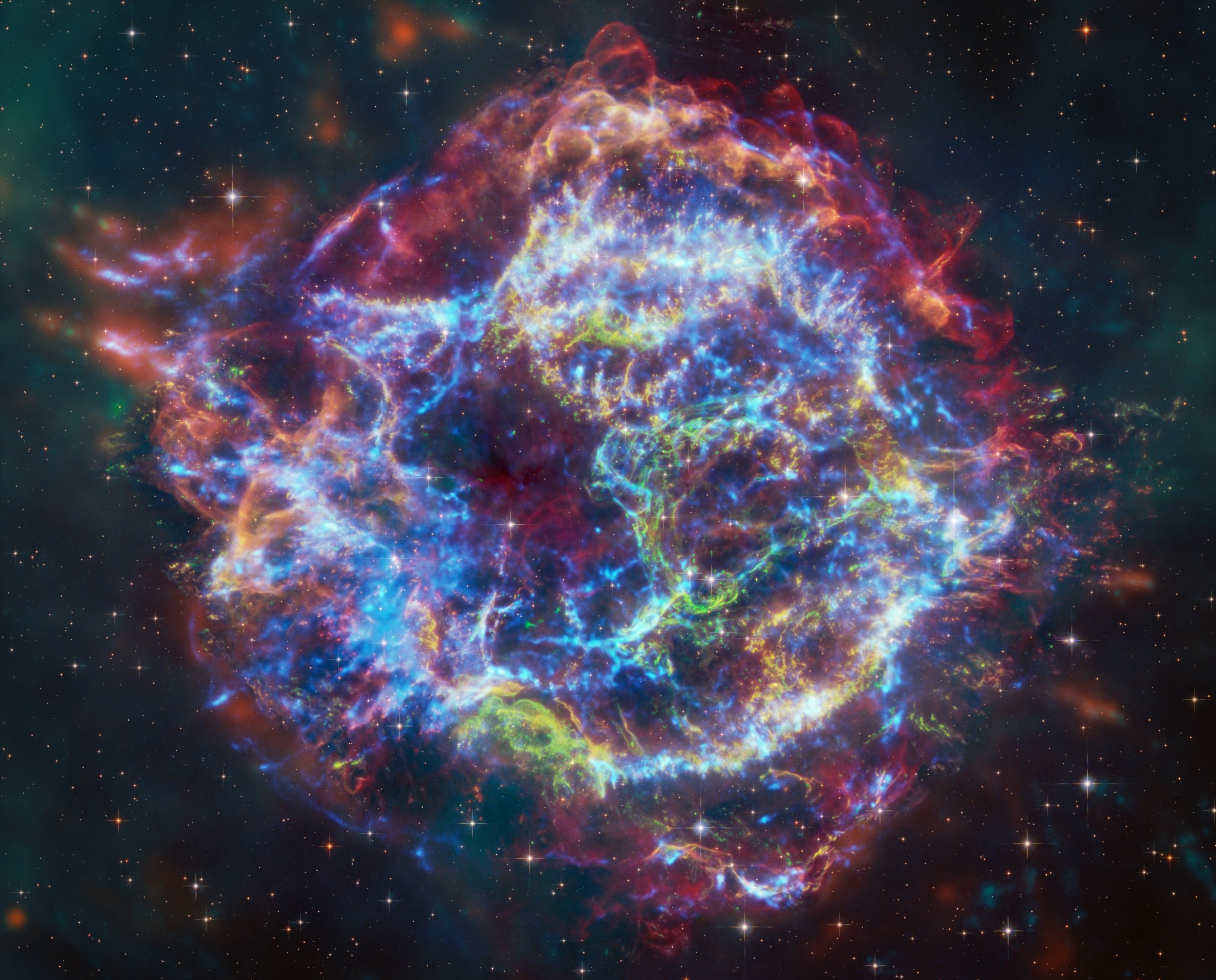 This image of Cassiopeia A resembles a disk of electric light with red clouds, glowing white streaks, red and orange flames, and an area near the center of the remnant resembling a somewhat circular region of green lightning. X-rays from Chandra are blue and reveal hot gas, mostly from supernova debris from the destroyed star, and include elements like silicon and iron. X-rays are also present as thin arcs in the outer regions of the remnant. Infrared data from Webb is red, green, and blue. Webb highlights infrared emission from dust that is warmed up because it is embedded in the hot gas seen by Chandra, and from much cooler supernova debris. Hubble data shows a multitude of stars that permeate the field of view.