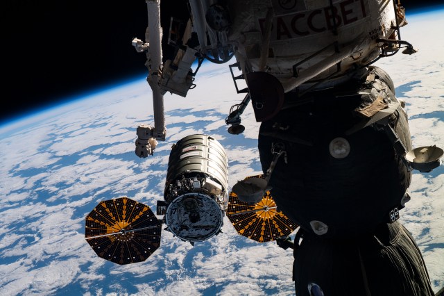 The Canadarm2 robotic arm is positioned to grapple the Northrop Grumman Cygnus cargo craft as it approaches its capture point with the International Space Station orbiting 255 miles above the Atlantic Ocean. Highlighting the foreground is the Soyuz MS-12 crew ship docked to the Rassvet module.