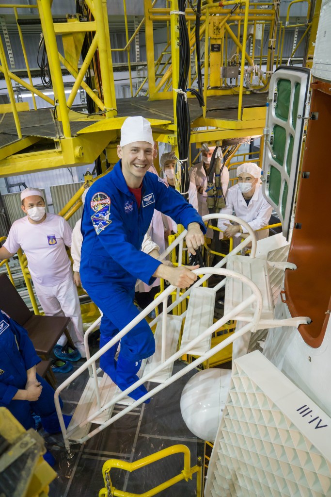 jsc2019e013413 (March 10, 2019) --- In the Integration Building at the Baikonur Cosmodrome in Kazakhstan, Expedition 59 crew member Nick Hague of NASA poses for pictures March 10 as he climbs aboard the Soyuz MS-12 spacecraft for final pre-launch preparations. Hague, Christina Koch of NASA and Alexey Ovchinin of Roscosmos will launch March 14, U.S. time, in the Soyuz MS-12 spacecraft from the Baikonur Cosmodrome for a six-and-a-half month mission on the International Space Station.