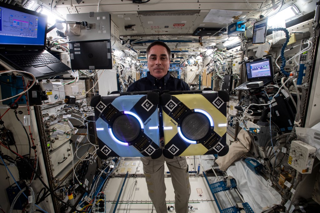 NASA astronaut and Expedition 63 Commander Chris Cassidy poses with two Astrobee robotic assistants during visual and navigation tests inside the Kibo laboratory module from JAXA (Japan Aerospace Exploration Agency).
