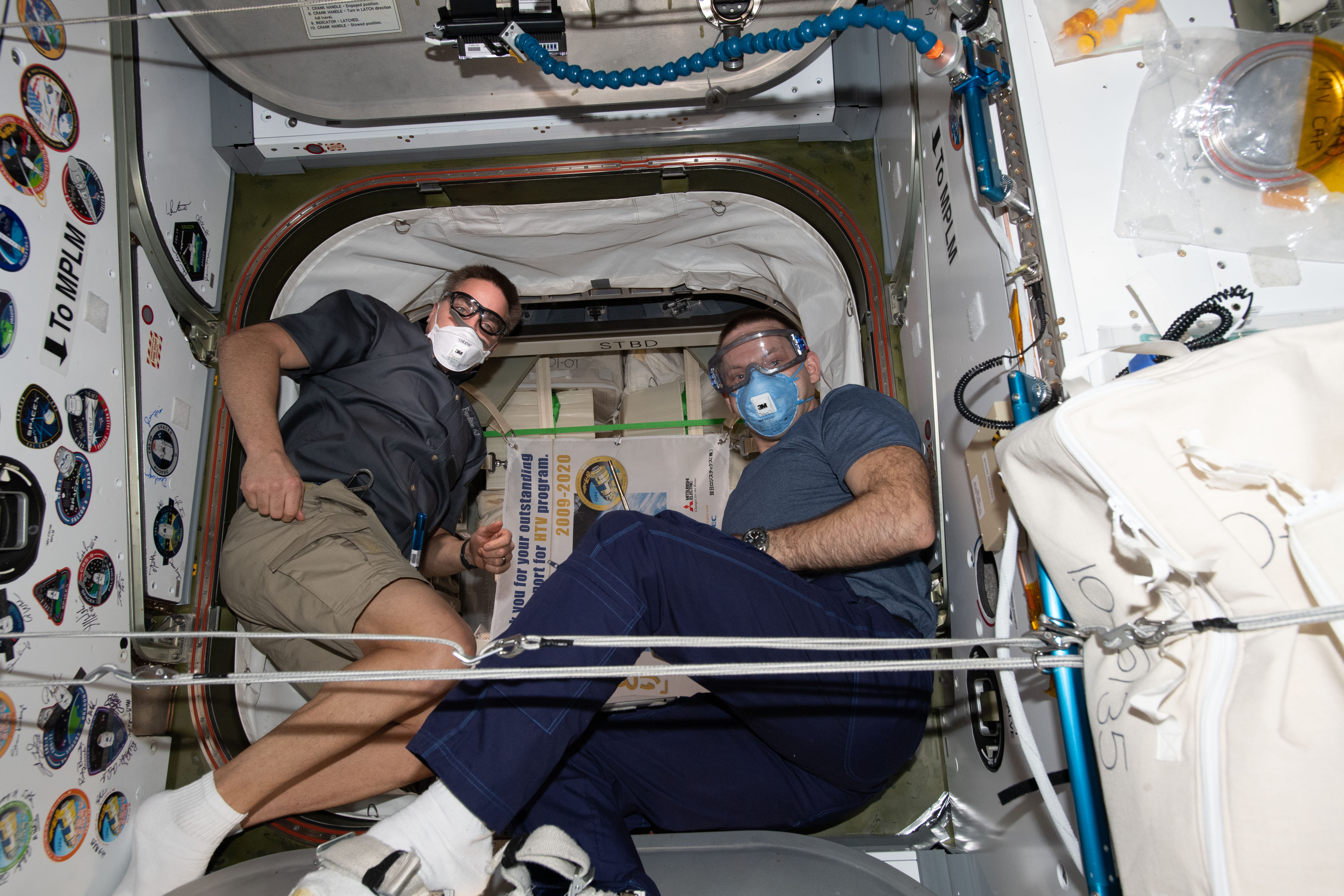 Expedition 63 crew members (from left) Chris Cassidy and Ivan Vagner wear personal protective equipment (PPE) before opening the hatch and entering Japan's resupply ship, the H-II Transfer Vehicle-9 (HTV-9). The PPE is necessary before entering a newly-arrived cargo craft to prevent dust and other irritants that may have become dislodged during the spacecraft's launch from entering the airways and the eyes.