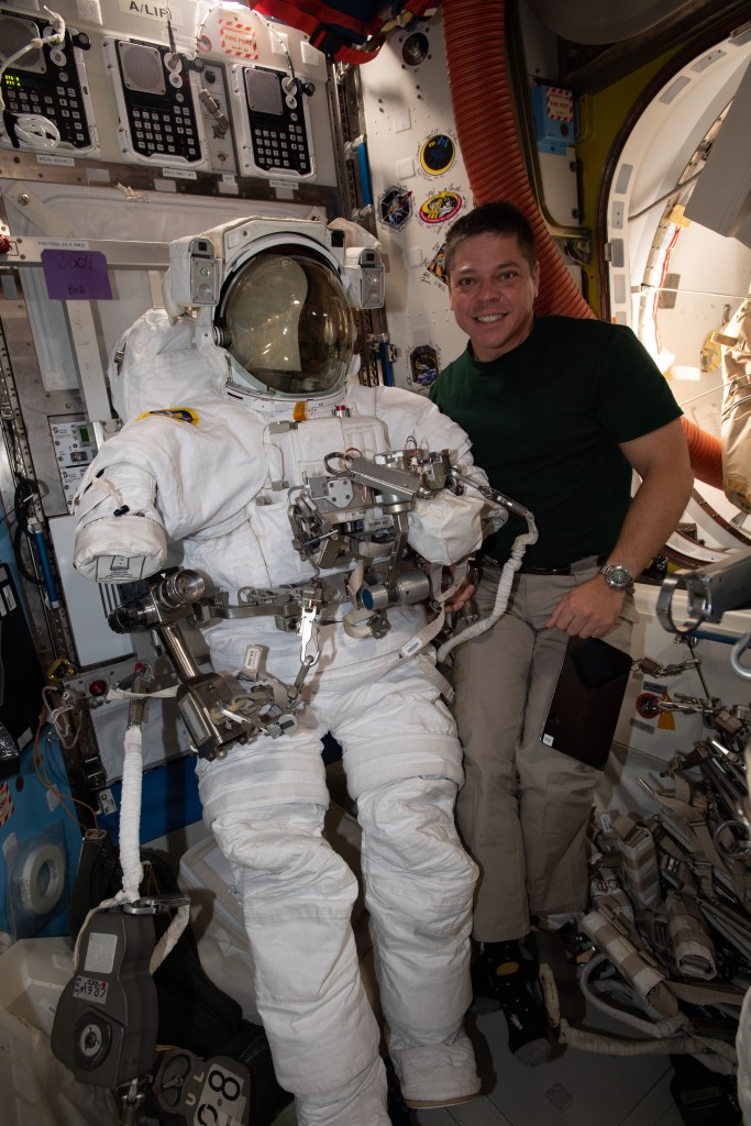 NASA astronaut and Expedition 63 Flight Engineer Bob Behnken poses with a U.S. spacesuit he is preparing for two spacewalks planned for June 26 and July 1 to upgrade power systems on the International Space Station.