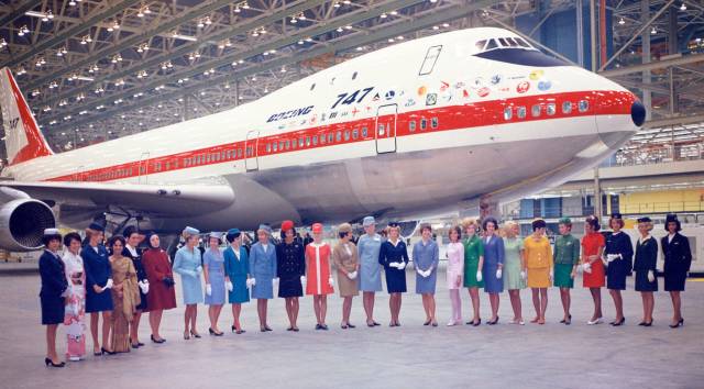 A Boeing 747 Jumbo Jet is seen in a hangar with 26 flight attendants representing 26 airliner standing in front of the airplane.