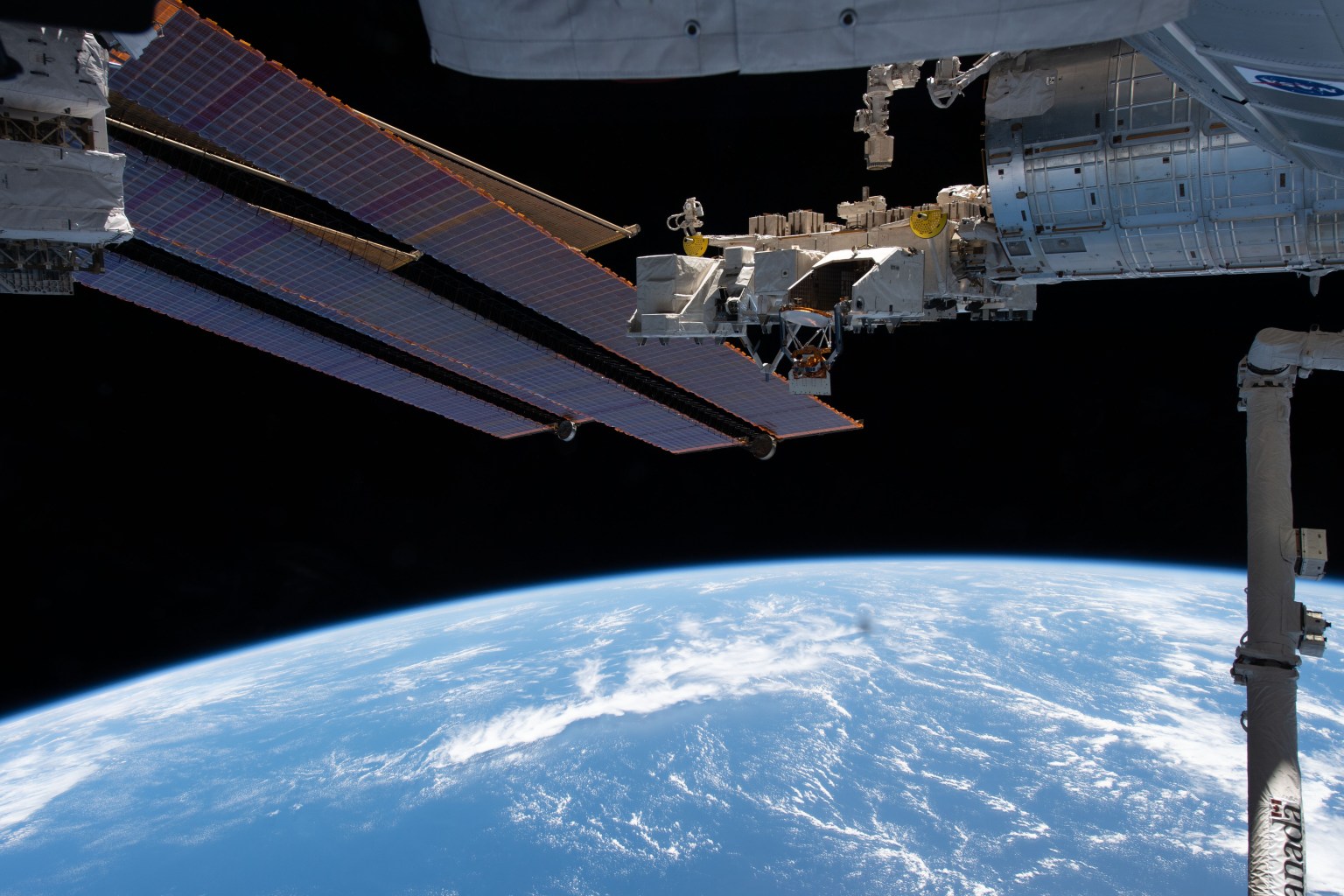 A set of the International Space Station's main solar arrays, slightly obscuring the smaller roll-out solar arrays, and the Kibo laboratory module with its exposed facility, a research platform that hosts external experiments, are pictured 261 miles above the Pacific Ocean.