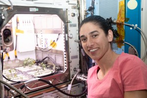 NASA astronaut and Expedition 70 Flight Engineer Jasmin Moghbeli poses in front of the Kibo laboratory module's Advanced Plant Habitat housing tomato plants for an experiment investigating how the plant immune system adapts to spaceflight and how spaceflight affects plant production.