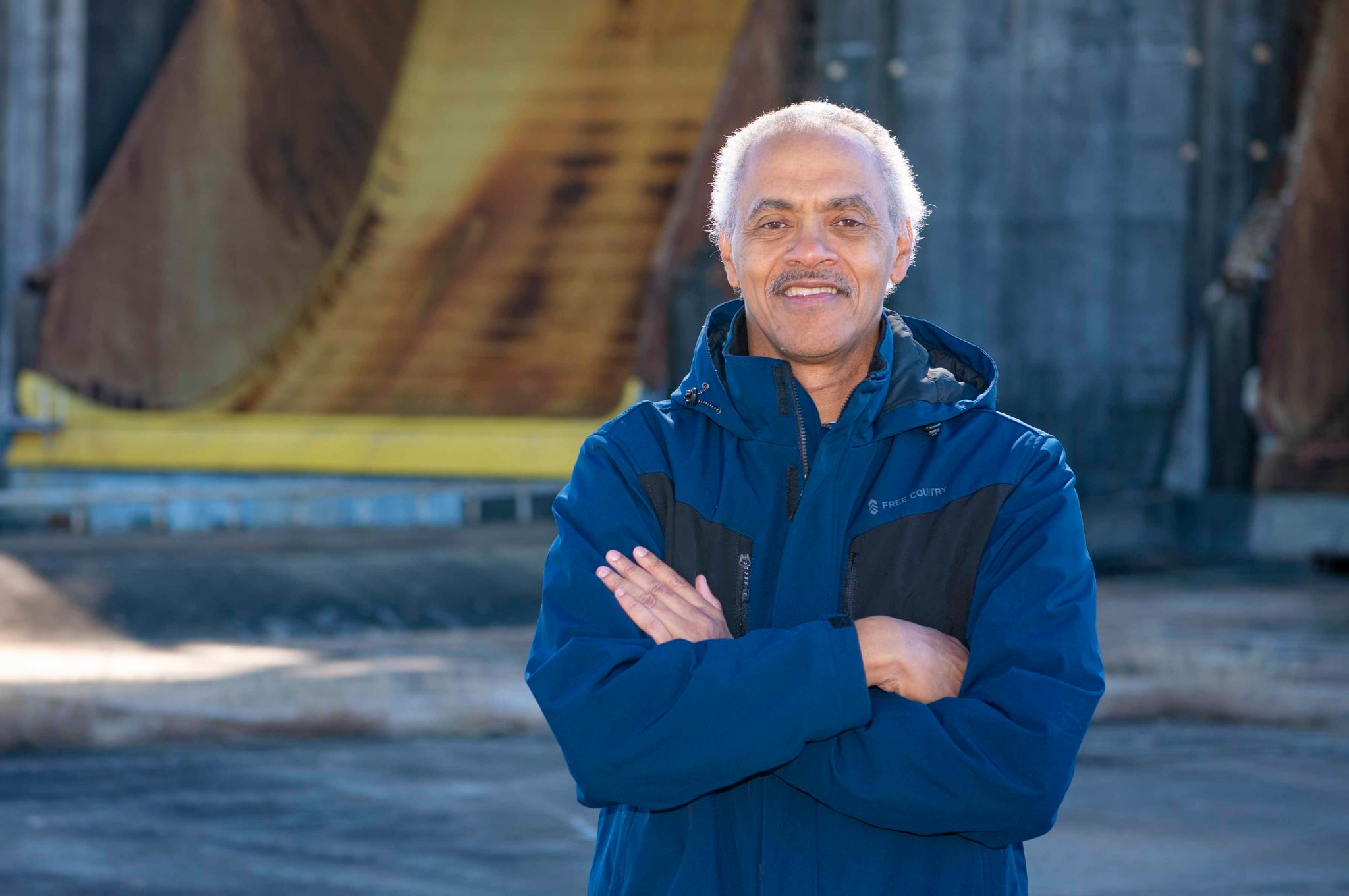 Maury Vander, wearing a navy-colored jacket, smiles at the camera. He is standing in the foreground with the Thad Cochran Test Stand in the background.