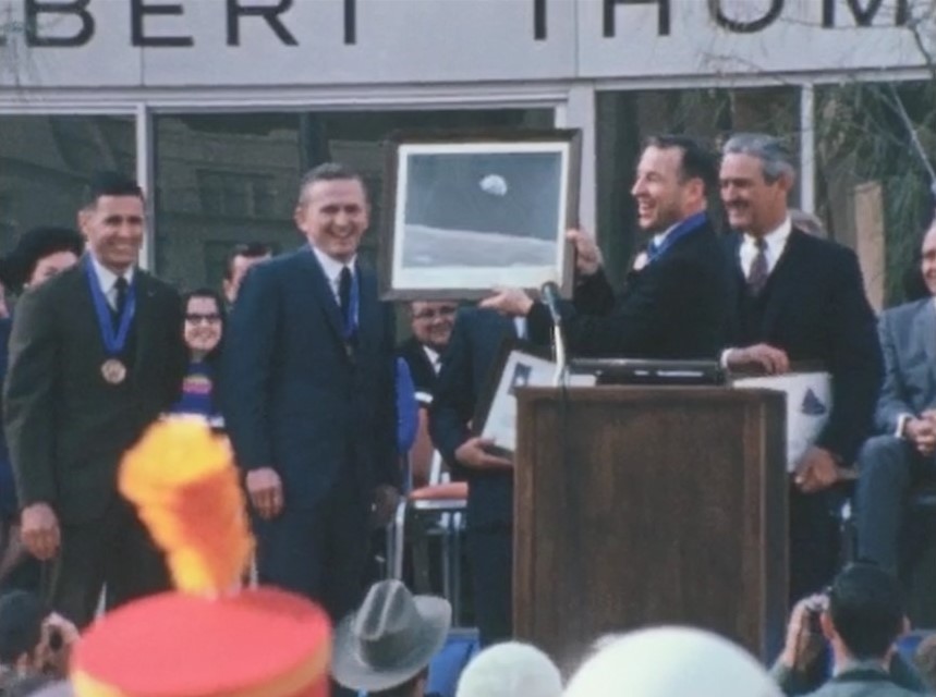 In Houston, Apollo 8 astronauts William A. Anders, left, Frank Borman, and James A. Lovell present an Earthrise photograph and flags of Texas to Governor John B. Connally, far right, and Mayor Louie Welch, hidden behind the photograph