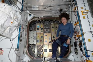 NASA astronaut and Expedition 61 Flight Engineer Jessica Meir poses in front of the closed hatch of the Cygnus space freighter from Northrop Grumman. Attached to the hatch is the SlingShot small satellite deployer loaded with eight CubeSats that were deployed into Earth orbit for communications and atmospheric research several hours after Cygnus departed the orbiting lab on Jan. 31, 2019.