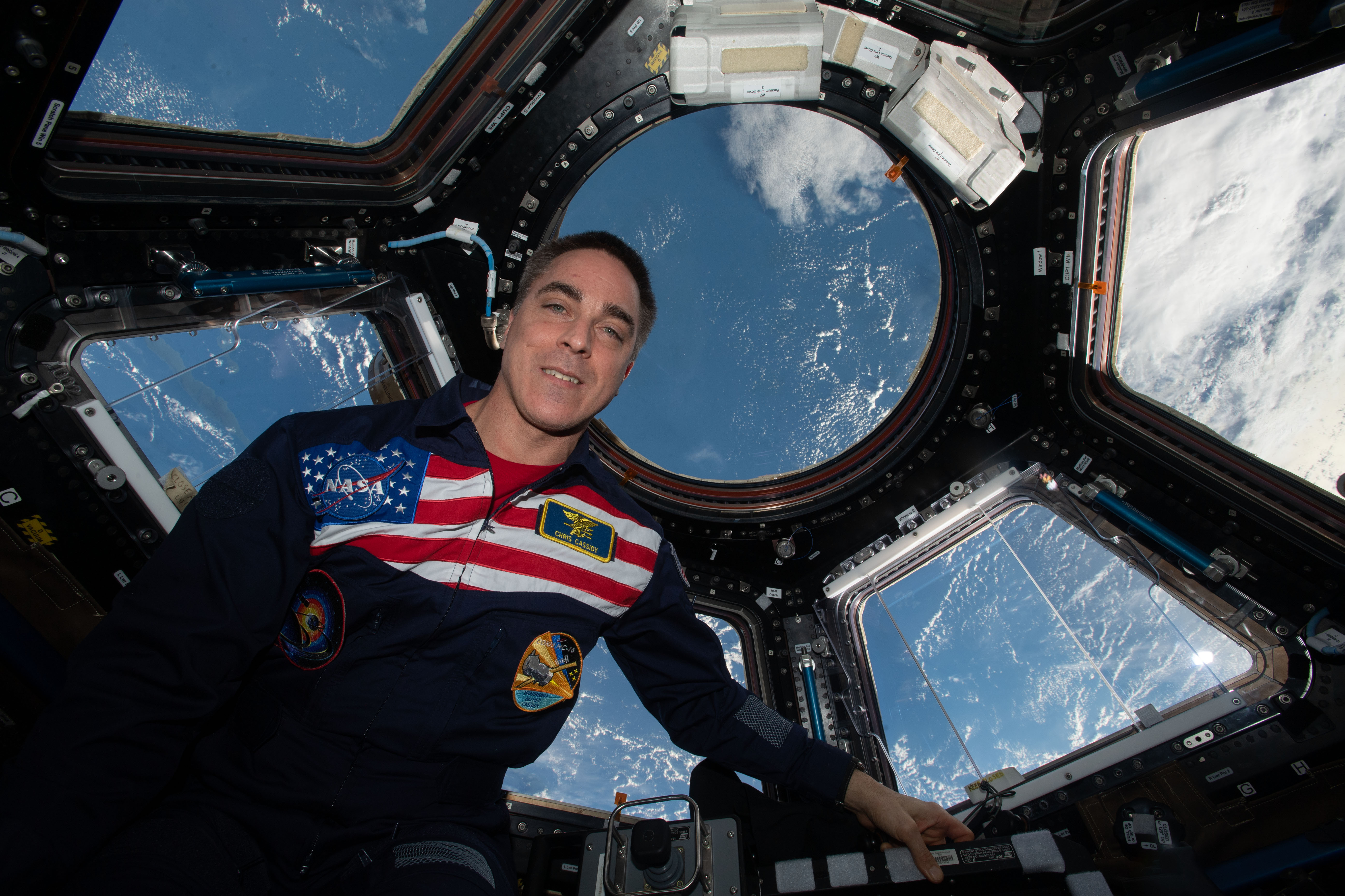 NASA astronaut and Expedition 63 Commander Chris Cassidy poses for a portrait wearing his flight suit inside the cupola, the International Space Station's window to the world. The orbiting lab was flying above the Pacific Ocean northeast of Papua New Guinea when this photograph was taken.