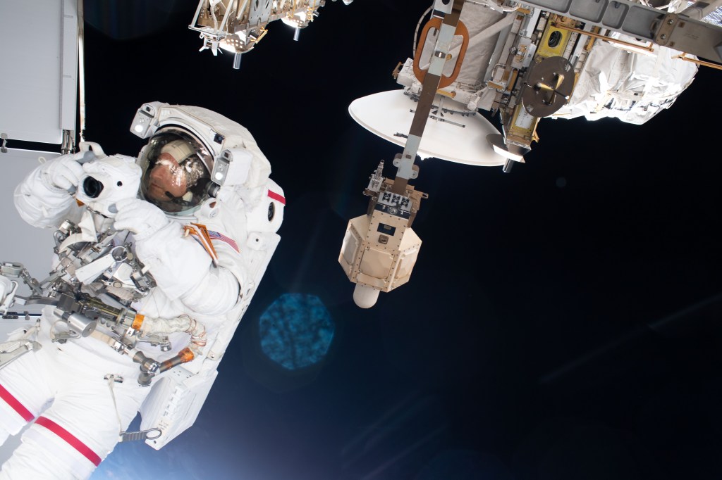 NASA astronaut Andrew Morgan takes pictures with a camera shielded from the effects of microgravity during a spacewalk to finalize thermal repairs on the Alpha Magnetic Spectrometer, a dark matter and antimatter detector.
