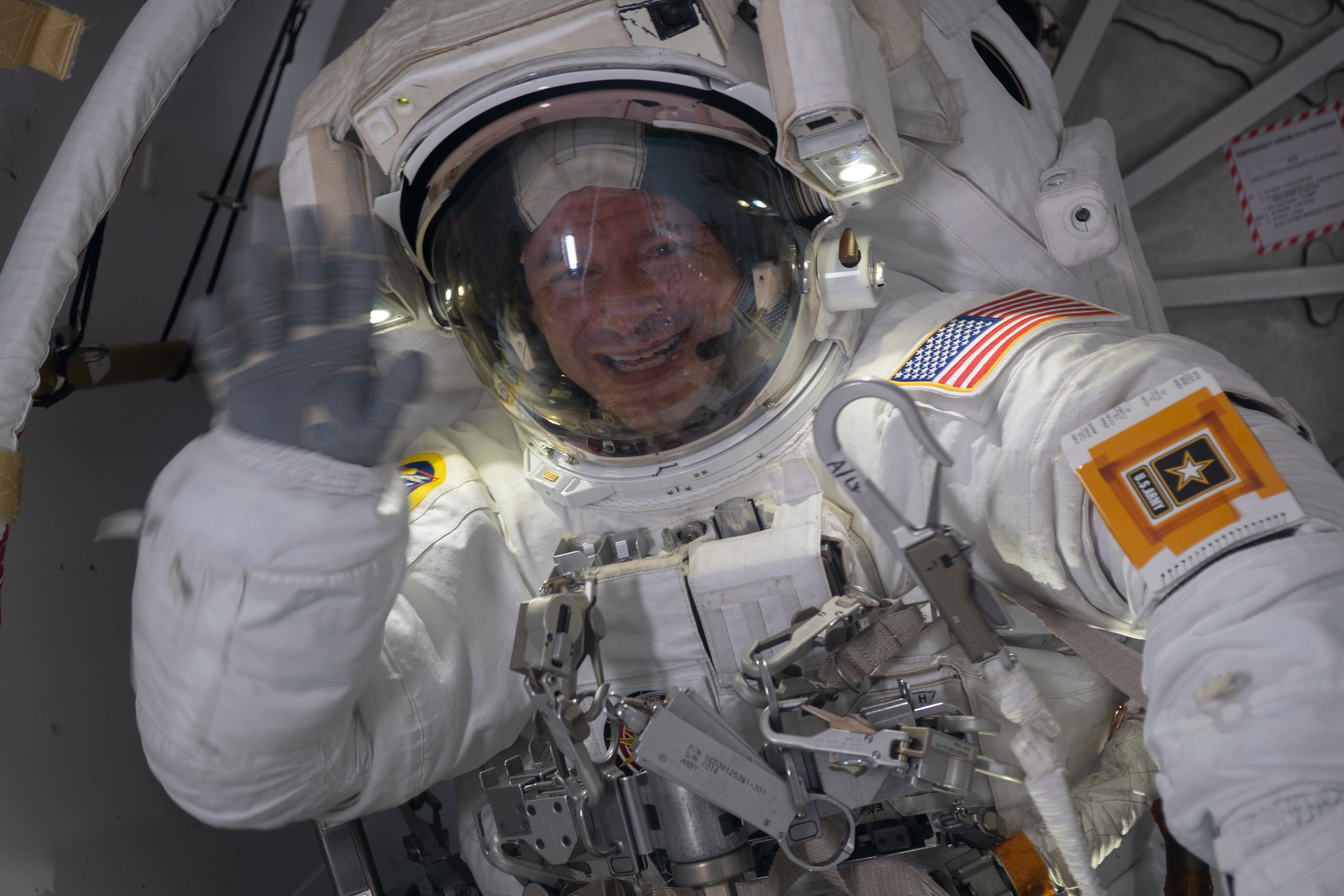 NASA astronaut Andrew Morgan waves from inside the crew lock portion of the Quest airlock where spacewalks in U.S. spacesuits are staged. He would go on to conduct a seven hour and one minute spacewalk with NASA astronaut Christina Koch to begin the latest round of upgrading the station's large nickel-hydrogen batteries with newer, more powerful lithium-ion batteries.