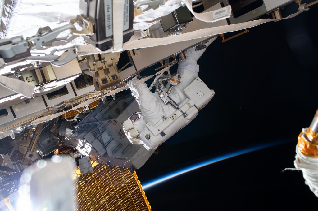 NASA astronaut Chris Cassidy works during a six-hour spacewalk to install lithium-ion batteries on the International Space Station's truss structure. The orbiting lab was above the north Pacific Ocean flying into a sunrise with a tiny waning crescent Moon in the background at the time this photograph was taken.