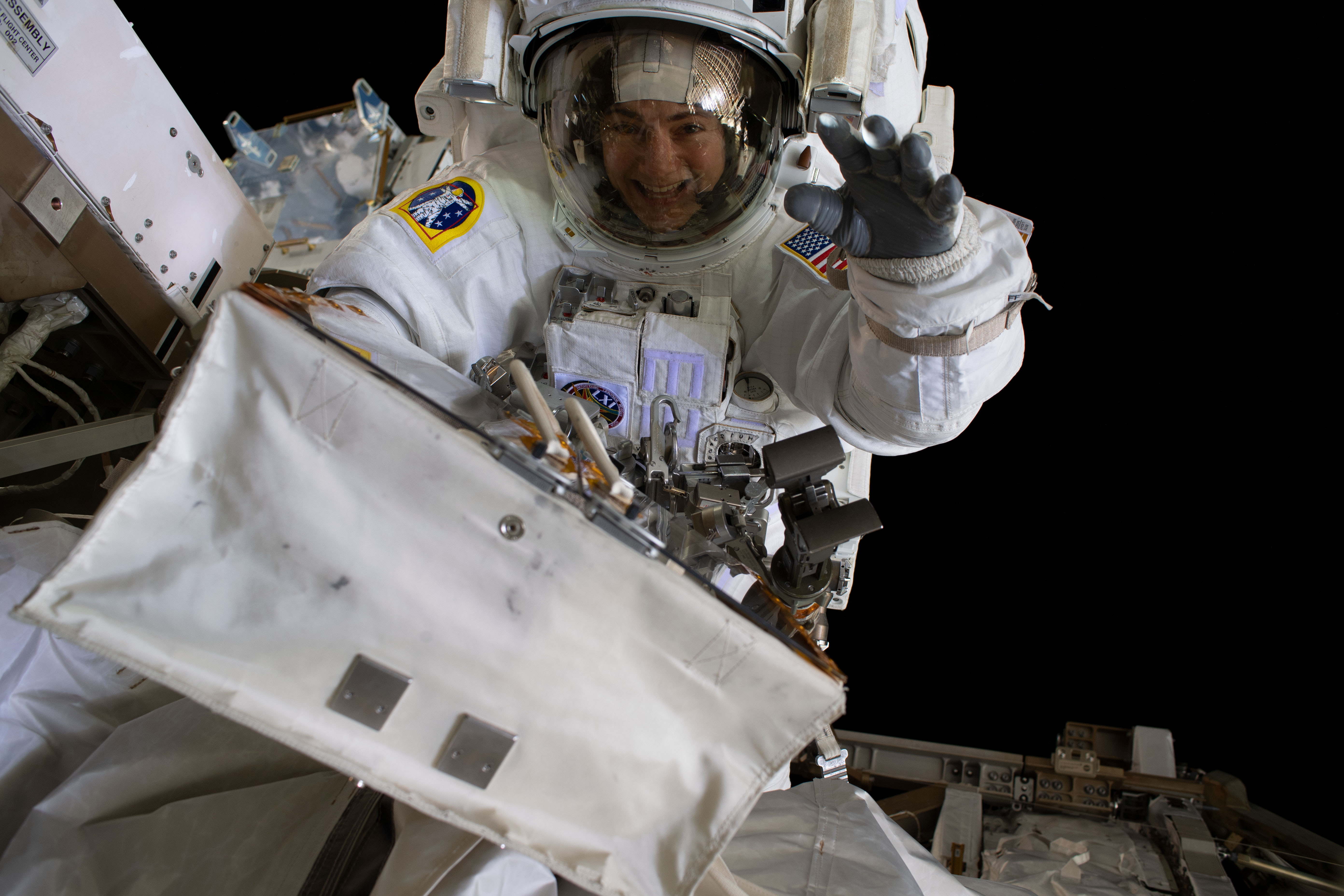 NASA astronaut Jessica Meir waves at the camera during a spacewalk with fellow NASA astronaut Christina Koch (out of frame). They ventured into the vacuum of space for seven hours and 17 minutes to swap a failed battery charge-discharge unit (BCDU) with a spare during the first all-woman spacewalk. The BCDU regulates the charge to the batteries that collect and distribute solar power to the orbiting lab’s systems.
