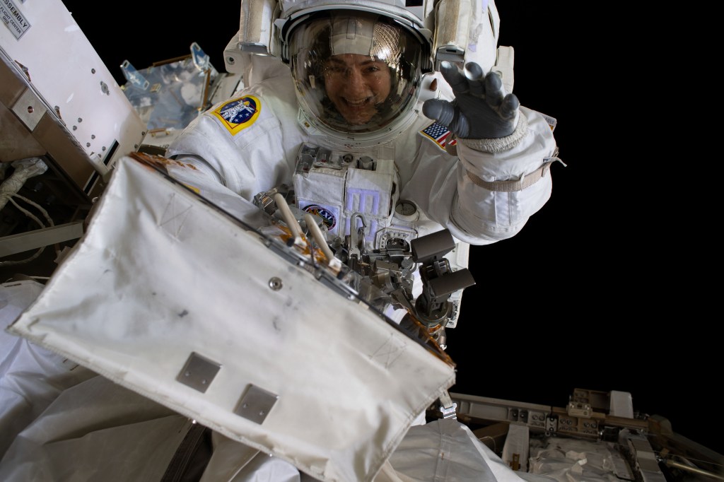 NASA astronaut Jessica Meir waves at the camera during a spacewalk with fellow NASA astronaut Christina Koch (out of frame). They ventured into the vacuum of space for seven hours and 17 minutes to swap a failed battery charge-discharge unit (BCDU) with a spare during the first all-woman spacewalk. The BCDU regulates the charge to the batteries that collect and distribute solar power to the orbiting lab’s systems.