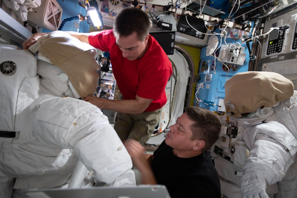 NASA astronauts (from top) Chris Cassidy and Bob Behnken work on U.S. spacesuits inside the International Space Station's Quest airlock.