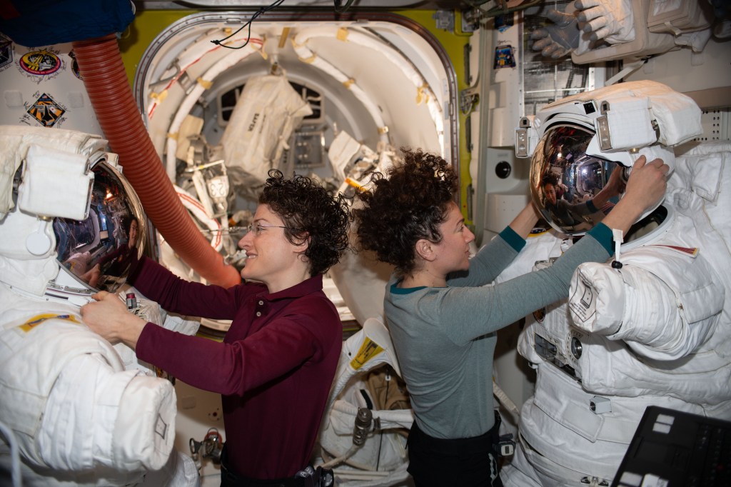 NASA astronauts Christina Koch (left) and Jessica Meir work on their U.S. spacesuits ahead of a spacewalk they conducted to install new lithium-ion batteries that store and distribute power collected from solar arrays on the station’s Port-6 truss structure.