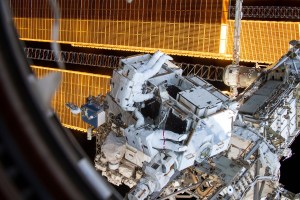 NASA astronauts Nick Hague (suit with no stripes) and Anne McClain (suit with red stripes) work to retrieve batteries and adapter plates from an external pallet during a spacewalk to upgrade the International Space Station's power storage capacity.