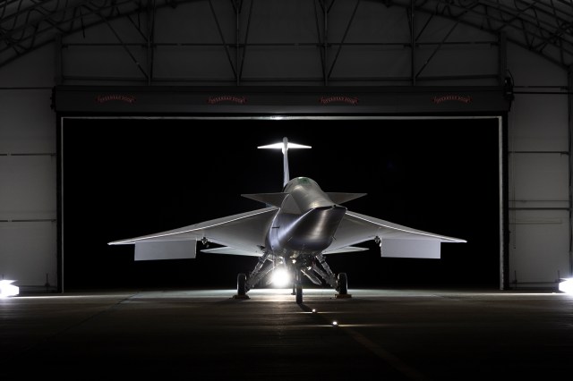 NASA's X-59 airplane sits in its hangar with lights shining on it.